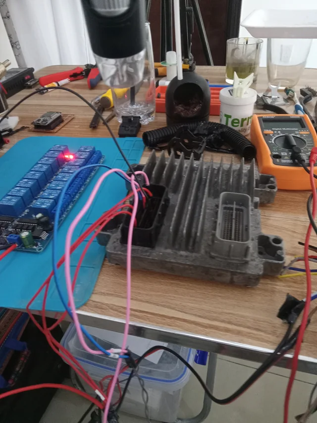 An automotive control unit connected to a relay board and measurement equipment on the electronics bench.