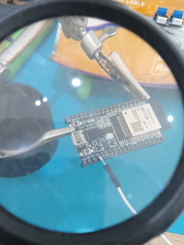 An ESP32 development board held under a magnifier for close hardware inspection and prototype wiring.